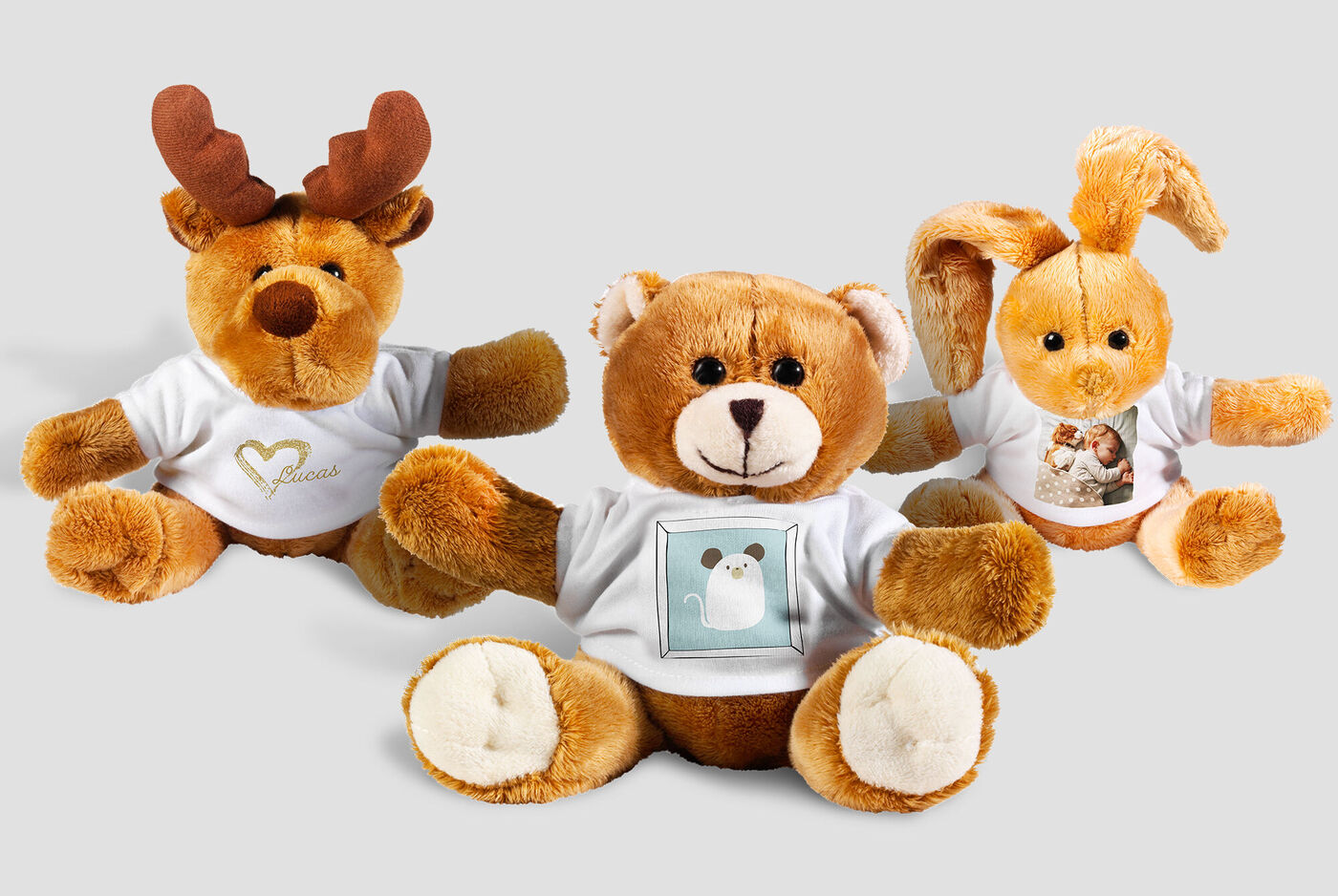 Tres suaves peluches: un reno, un oso y un conejo, usando camisetas lindas.
