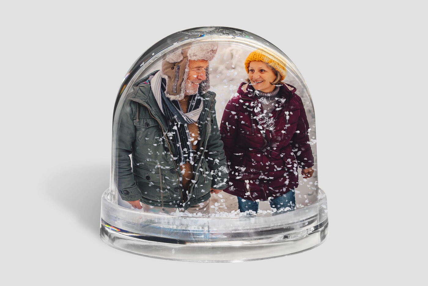 Una pareja feliz en una bola de nieve, paseando juntos. El hombre lleva una chaqueta verde y un sombrero cálido, la mujer un bufanda colorida.